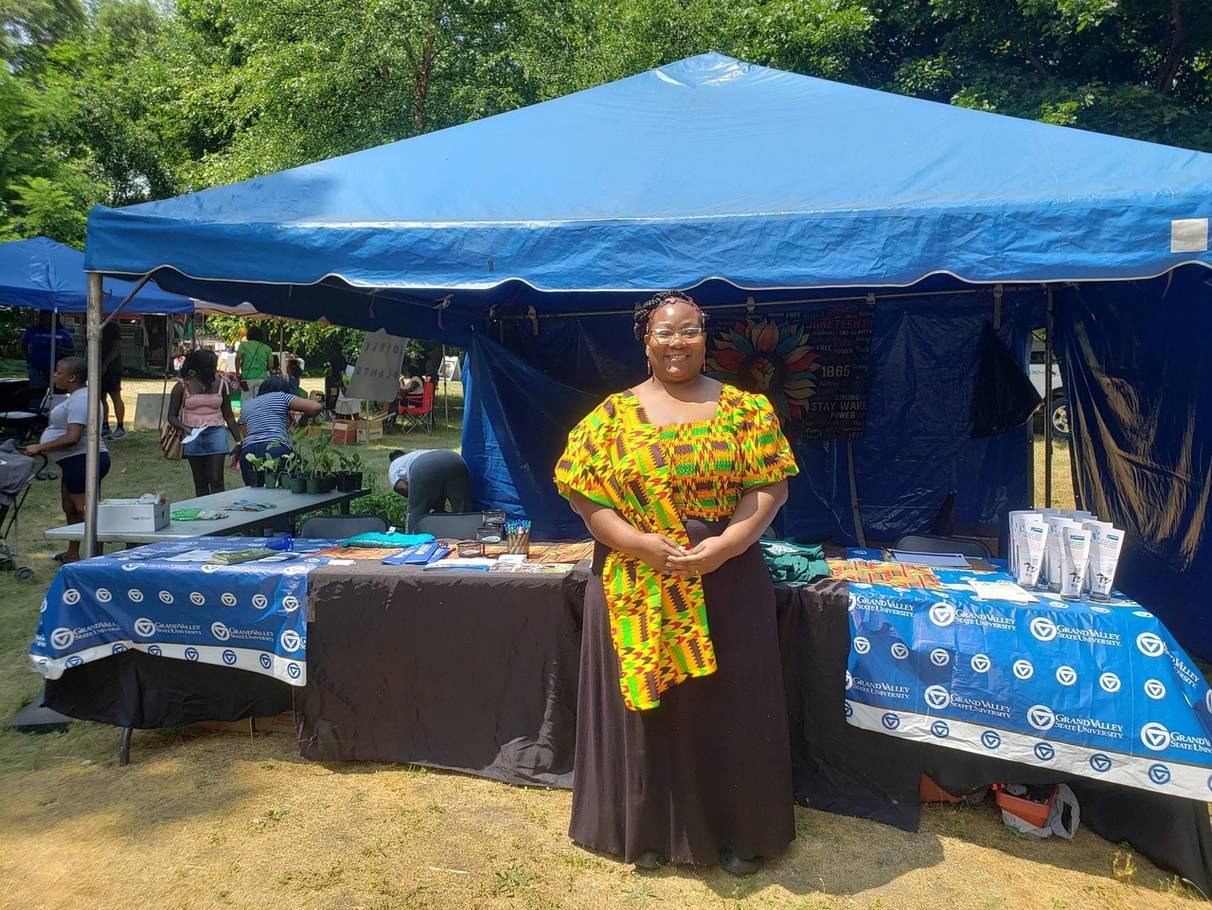 woman in African garb standing in front of a long table with a blue canopy over it